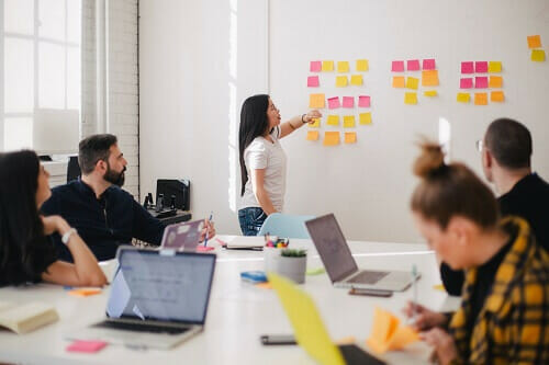 Woman presenting a plan with sticky notes on a wall board in a meeting room