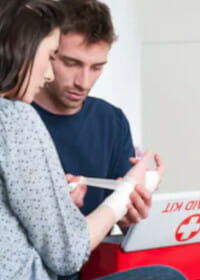 A man applying medical tape to a woman's right hand using a medical kit in a clinical setting