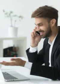 Man in a suit talking on the phone while looking at his laptop in an office